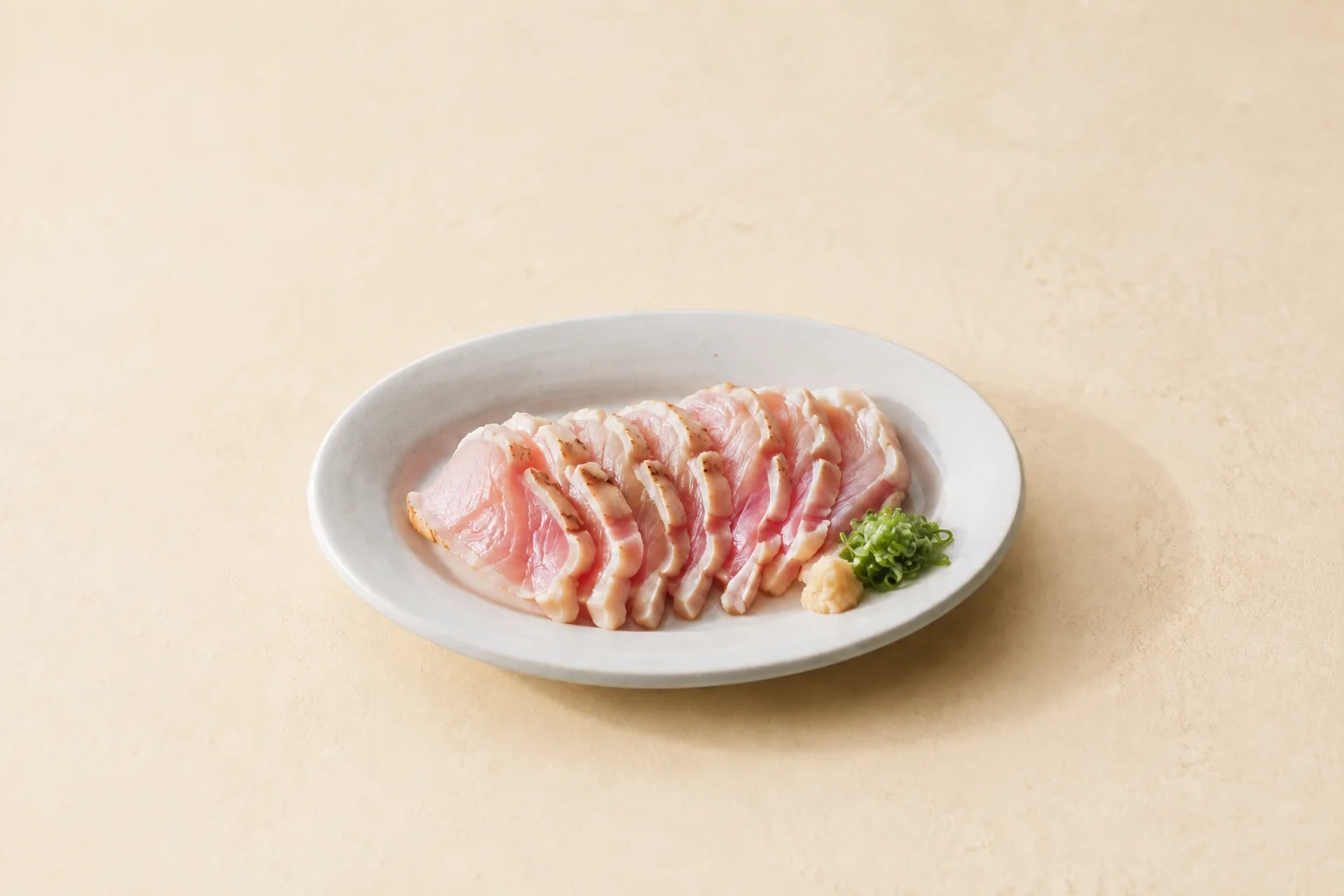 淡いクリーム色のテーブルに置かれた鶏たたきの皿。記事のイメージ画像